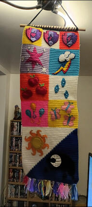 A crocheted tapestry featuring the cutie marks of the cutie mark crusaders, the mane 6 and the princesses from My Little Pony