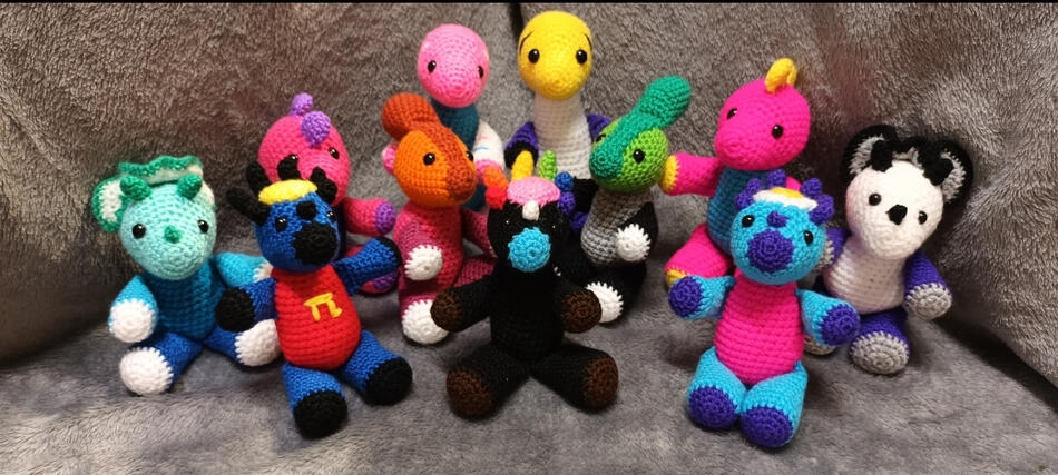 Various crocheted dinosaurs in the colours of different pride flags.