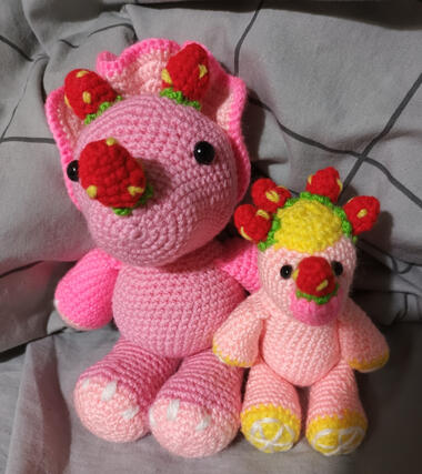 2 crocheted plushies of dinosaurs in a strawberry colour pallete.