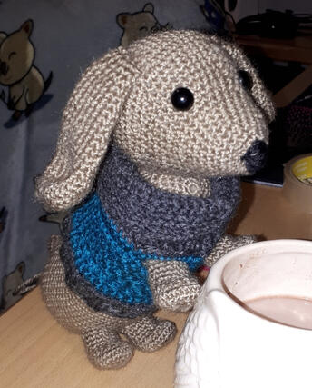 A crocheted plushie of a Sausage Dog wearing a blue jumper)