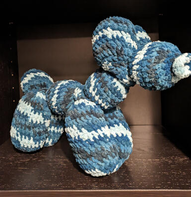 A crocheted stuffed animal designed to look like a balloon dog. It is various shades of blue.