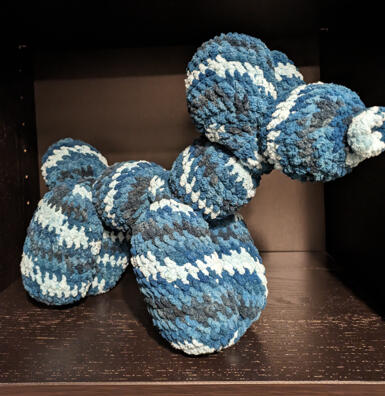 A crocheted stuffed animal designed to look like a balloon dog. It is various shades of blue.