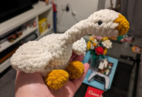 A crocheted goose with a white body, yellow beak and yellow feet.